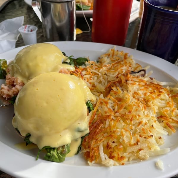 Two eggs benedict with hollandaise sauce and hash browns on a white plate at Sunnyside Cafe.