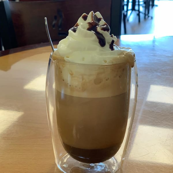 A Sunnyside Cafe mocha with whipped cream and chocolate drizzle in a clear glass.