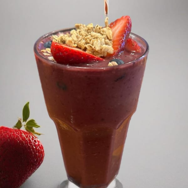 A berry smoothie with granola, strawberries, and blueberries, with a fresh strawberry beside it.