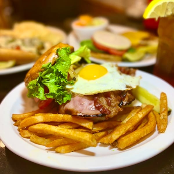 A burger with bacon, fried egg, lettuce, and fries on a white plate.