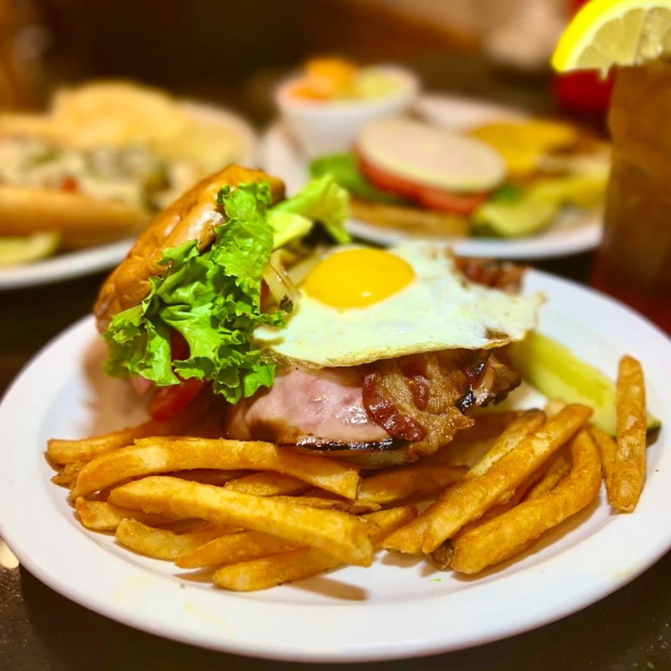 A burger with bacon, fried egg, lettuce, and fries on a white plate.