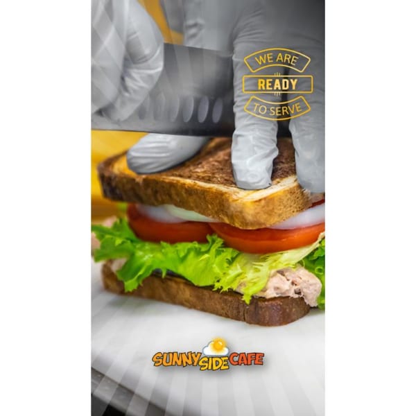 Gloved hands slicing a tuna sandwich with lettuce, tomato, and onion, with the Sunnyside Cafe logo.