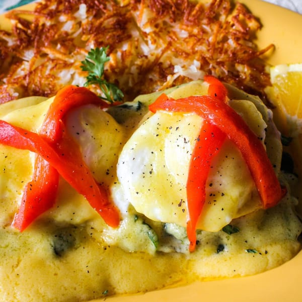 Sunnyside Cafe's Eggs Benedict with red peppers, hollandaise sauce, and hash browns on a yellow plate.
